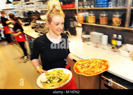 Kellnerin trägt Pizza in der Tabelle in eine Pizzeria in England Stockfoto