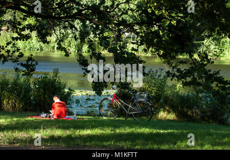 Eine Frau liest Buch neben dem Teich im Schloss Charlottenburg in Berlin sitzen. Stockfoto