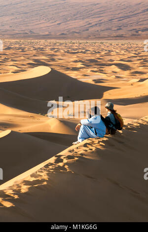 Marokko, Mhamid, Erg Chigaga Sanddünen. Sahara. Lokale Berber Mann, Reiseführer, und Touristische, Frau, auf Sand dune. Stockfoto