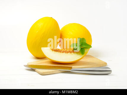 Ganze zwei gelbe Melonen und Stück Melone neben sie auf Schneidebrett Stockfoto