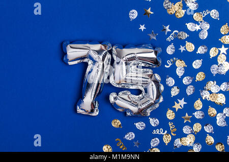 Silberne Folie Nr. 75 Ballon auf einem blauen Hintergrund mit Glitzer gonfetti Stockfoto