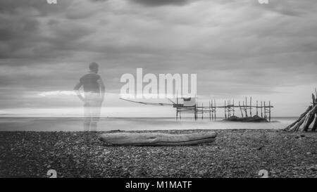 Eine Person auf Punta Aderci' s Beach ein Naturschutzgebiet in Vasto, Abruzzen, Italien. Im Hintergrund unter einem stürmischen Himmel eine trabucco typische Angeln Maschine Stockfoto