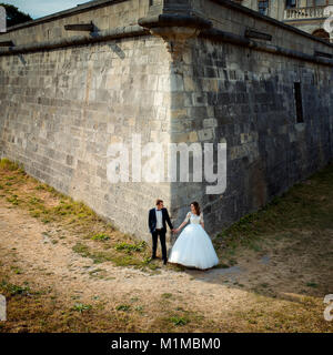 Jungvermählten sind, Hände halten, während in der Ecke des riesigen Mauern der alten barocken Schloss steht. Stockfoto