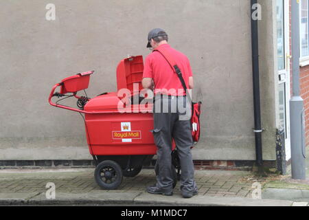 Eine rote ROYAL MAIL TROLLEY WARENKORB MIT ARBEITER SORTIERUNG MAIL IN EINER STRASSE IN FLEETWOOD STADTZENTRUM Stockfoto