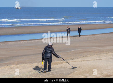 Ältere Frau mit Metalldetektor beachcombing am Sandstrand entlang der Nordseeküste im Winter Stockfoto