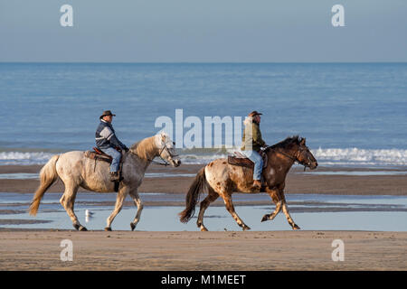 Ältere Paare Reiten am Sandstrand entlang der Nordseeküste an einem kalten Tag im Winter Stockfoto