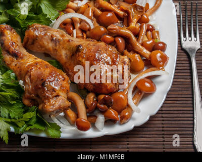 Im Ofen gebacken, das Huhn drumstick liegt auf einem weißen Teller mit eingelegte Pilze, Petersilie, gehackten Zwiebeln, Gewürze Stockfoto