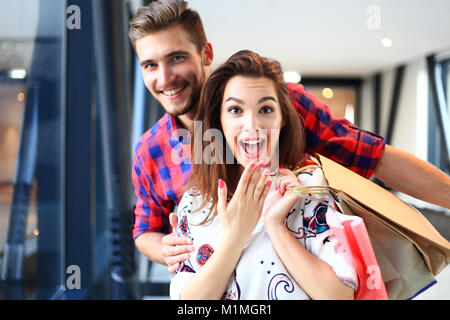 Verkauf, Konsumismus und Personen Konzept - glückliches junges Paar mit Einkaufstaschen wandern in der Mall. Stockfoto