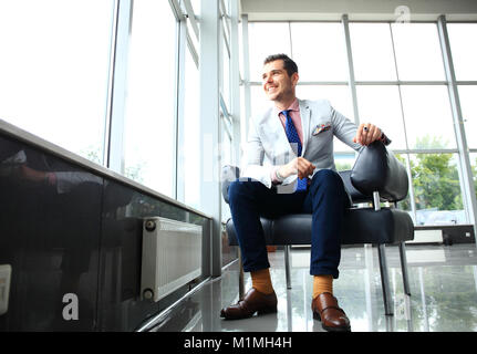 Low Angle Shot der ein hübscher junger Geschäftsmann in einem stilvollen, modernen Büroflächen mit großen Fenstern. Stockfoto