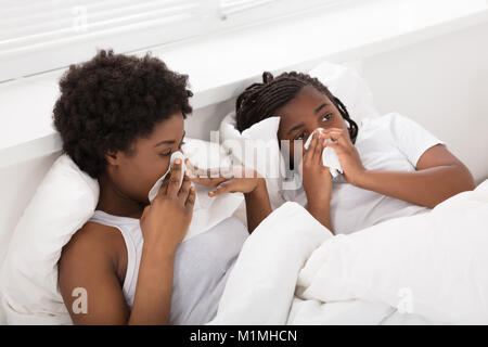Mutter und Tochter liegend auf Bett Niesen in Geweben Stockfoto