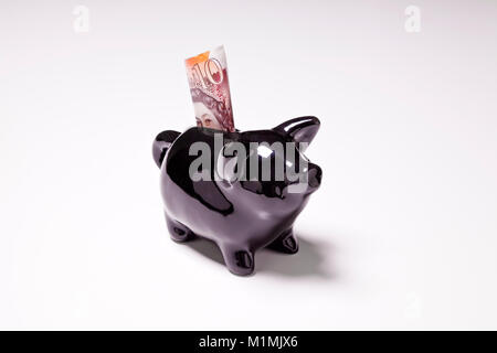 Schwarzer Keramik Sparschwein mit gefalteten £ 10 Hinweis auf weißem Hintergrund Stockfoto