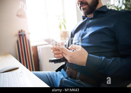 Unternehmer im Rollstuhl mit Smartphone in seinem Büro. Stockfoto