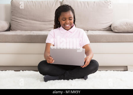 Portrait eines glücklichen Mädchen sitzen auf dem Teppich mit Laptop zu Hause Stockfoto