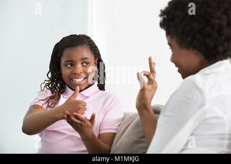 Lächelnde junge Mutter lernen Gebärdensprache zu sprechen mit ihrer Hörbehinderung Tochter Stockfoto