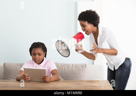 Mutter an ihre Tochter Holding digitale Tablette in ein Megaphon zu Hause Schreien Stockfoto