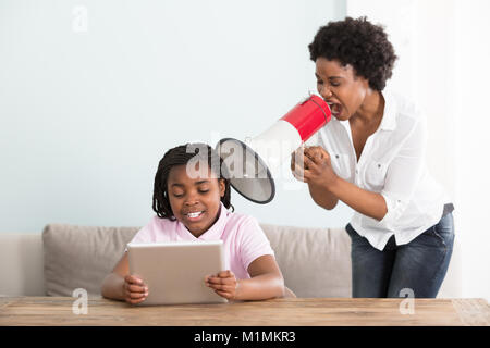 Mutter an ihre Tochter Holding digitale Tablette in ein Megaphon zu Hause Schreien Stockfoto