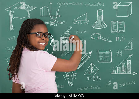 Nahaufnahme der lächelnde Mädchen Zeichnung pädagogische Symbole mit Kreide auf grüner Tafel Stockfoto