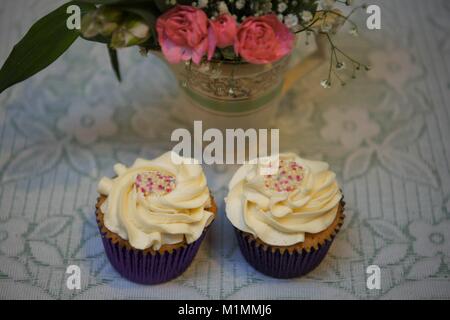 Leckere Vanille Creme Cupcake auf einem Vintage altmodischer Spitze Tischdecke und Blumen Teekanne im Hintergrund mit frischen Blumen Stockfoto