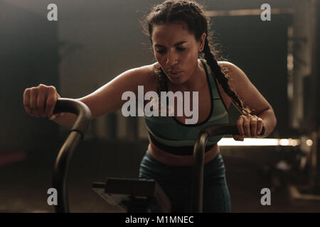 Passen junge Frau mit Fahrrad an der Turnhalle. Fitness weibliche mit Air Bike für cardio Workout im Fitnessraum. Stockfoto