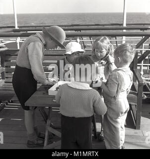 1950, historische, auf dem Ozean, an Bord eines Dampfers Union-Castle vorangegangen für ein neues Leben in Südafrika, eine Gruppe junger Kinder spielen zusammen mit kleinen Bauunternehmen hat sich Kunststoff Spielzeug auf einem kleinen Tisch draussen auf dem Deck des Schiffes. Stockfoto