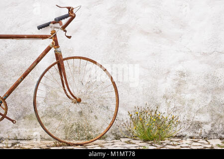 Detail des alten, rostigen verlassenen Fahrrads, das sich gegen eine Steinmauer lehnt Stockfoto