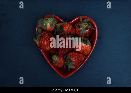 Herzförmige Schale voller Frische Erdbeeren auf schiefertafel Hintergrund. Flach, Ansicht von oben. Stockfoto