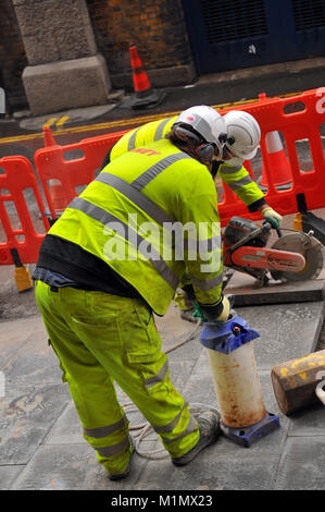 Bau- oder Autobahnen Arbeitnehmer Festlegung der Pflastersteine und die Instandsetzung der Wanderwege und Straßen mit leistungsstarken Power Tools in Central London gelb tragen. Stockfoto