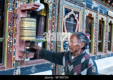 Jakar, Bumthang, Bhutan. Mann Drehen einer Gebetsmühle, als er von einem Store Eingang geht. Stockfoto