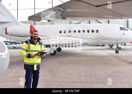 Portrait einer flugzeugmechaniker in einem Hangar mit Jets am Flughafen - Kontrolle der Flugzeuge für Sicherheit und Technische Funktion Stockfoto