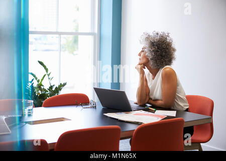 Frau mittleren Alters Blick aus dem Fenster in den Sitzungssaal Stockfoto