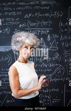 Akademische Frau mittleren Alters an der Tafel lächelnd in die Kamera Stockfoto