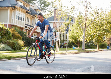 Vater Radfahren entlang der Straße mit Tochter im Kindersitz Stockfoto