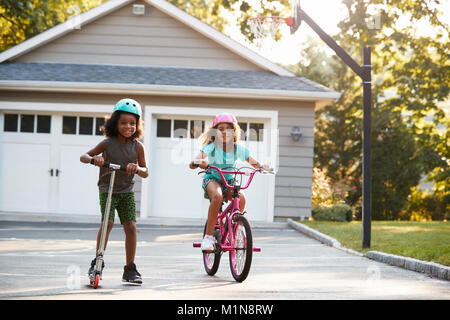 Mit Bruder Reiten Roller und Fahrrad in der Einfahrt zu Hause Schwester Stockfoto