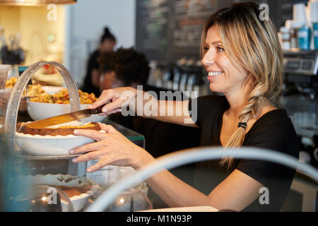 Kellnerin hinter Zähler in Coffee Shop Schneiden Stück Kuchen Stockfoto