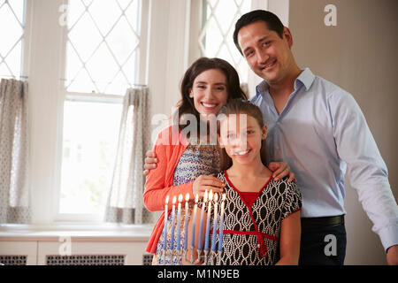 Jüdische Eltern und Tochter lächelnd, angezündete Kerzen auf menorah Stockfoto