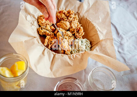 Eine Hand mit einer Gabel ein zerschlagener Oyster aus einem Pergament-line Warenkorb auszuwählen, mit Sauce gribiche Stockfoto