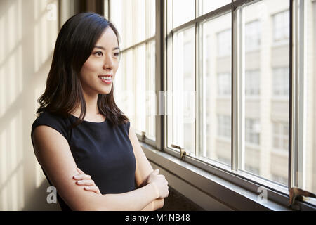 Lächelnde junge chinesische Geschäftsfrau Blick aus Fenster Stockfoto