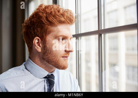 Junge Rothaarige bärtige Geschäftsmann Blick aus Fenster Stockfoto
