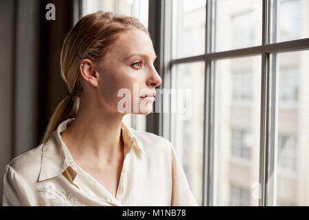Blonde junge geschäftsfrau Blick aus Fenster Stockfoto