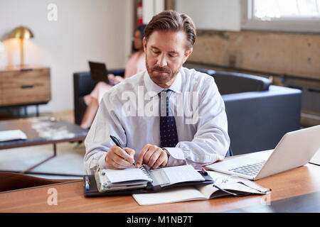 Geschäftsmann am Schreibtisch Schreiben von Notizen Stockfoto