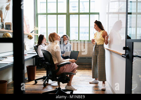 Frau, die an der Tafel in einer Sitzung mit weiblichen Team Stockfoto