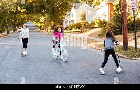 Drei Mädchen reiten auf Roller und ein Fahrrad auf der Straße Stockfoto