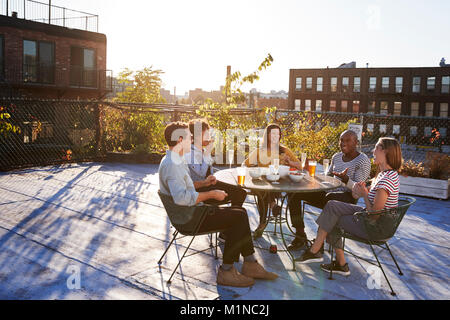 Fünf Freunde sitzen im Gespräch an einem Tisch auf einem New York Dachterrasse Stockfoto