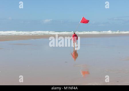 Ein kornisches Rettungsschwimmer Positionierung eine rote Flagge für Schwimmer und Surfer von gefährlichen Bedingungen auf Mawgan Porth Strand warnen, Cornwall, England, Großbritannien. Stockfoto