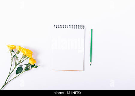Kleine gelbe Rosen und Notebook mit Bleistift auf White Table Top View Stockfoto