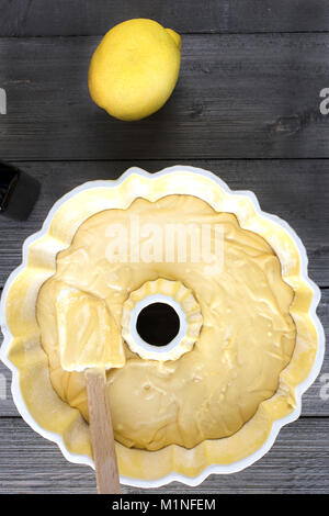 Zubereitung von Teig für einen Zitronenkuchen in einem gelben bundt Wanne mit einem Spachtel auf einer rustikalen Tisch Stockfoto