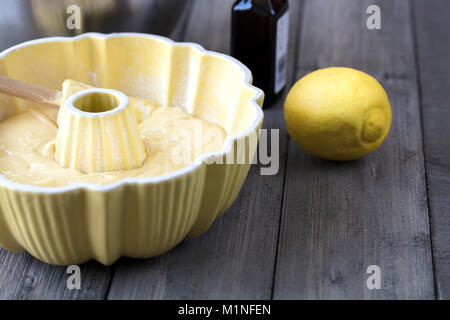 Zubereitung von Teig für einen Zitronenkuchen in einem gelben bundt Wanne mit einem Spachtel auf einer rustikalen Tisch Stockfoto