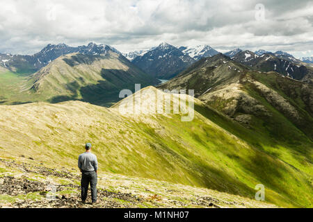 Ein Wanderer sieht auf den malerischen Blick auf die Chugach Mountains von Rendevous Peak in der South Fork von Eagle River Valley in der Chugach State Park in Alaska. Stockfoto