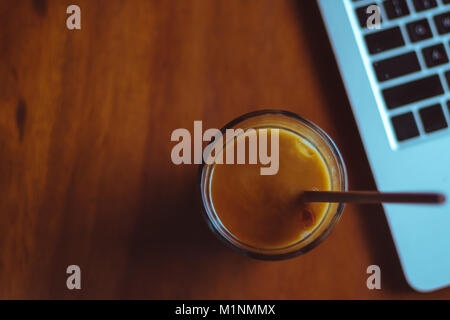 Eis Kaffee in der Nähe von Laptop auf einem Holztisch Stockfoto