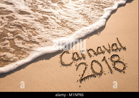 Nachricht für Karneval 2018 geschrieben auf einer glatten Sandstrand mit einer schaumigen ankommenden Welle Stockfoto